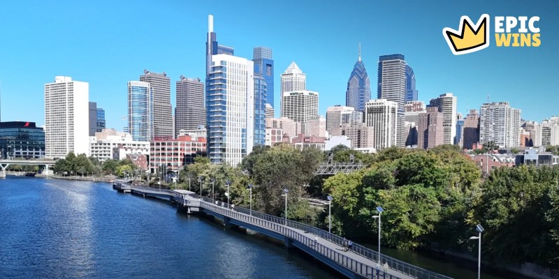 Philadelphia skyline and riverside boardwalk under a blue sky, with the EpicWins logo